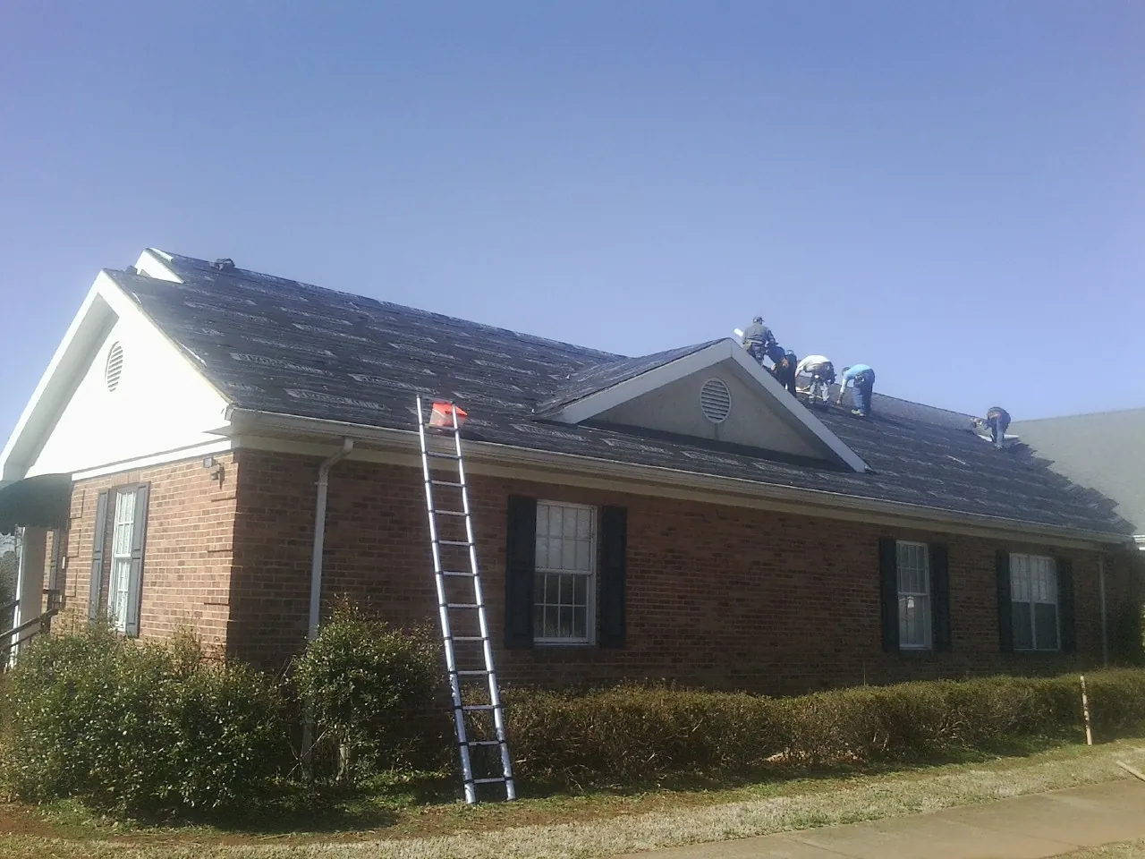Crew tearing shingles off a brick ranch roof with a ladder set — Metal Roof Repair work by our crew in Nampa
