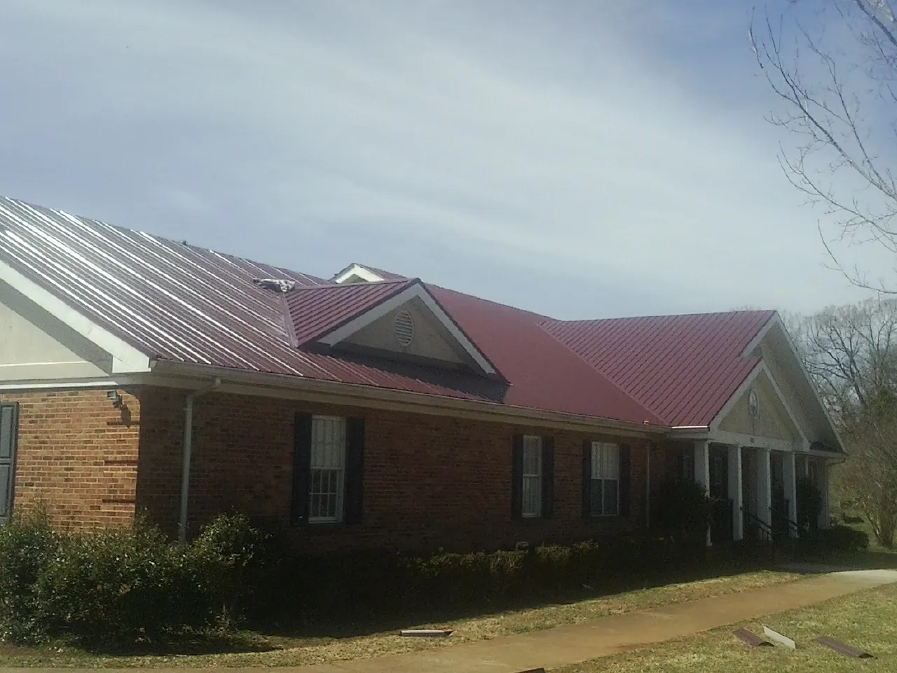 Red metal roof with gabled entries on a long brick building, from a Hail Damage Roof Repair job in Nampa