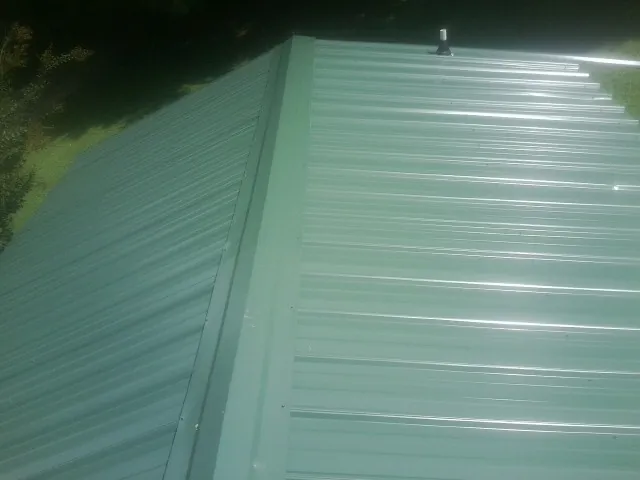 New green metal panels meeting at the ridge of a roof — Flat Roof Repair work by our crew in Nampa