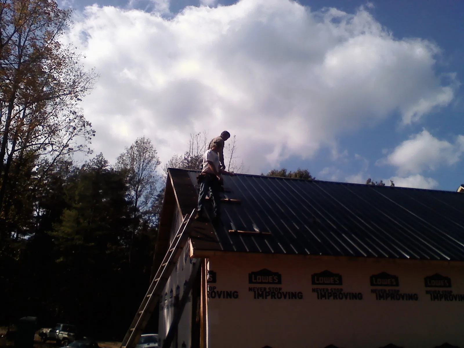 Roofer fastening dark metal panels high against a cloudy sky, from a Roof Inspection job in Nampa