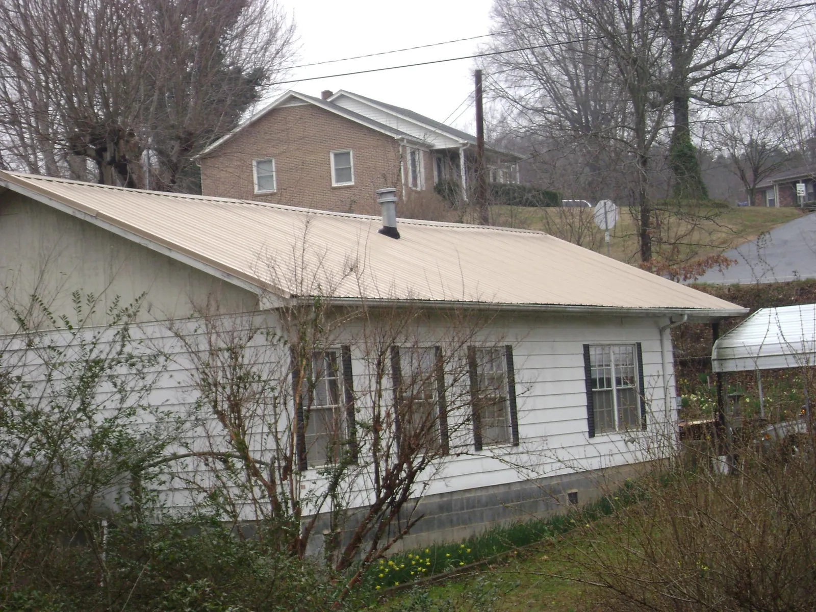 Tan metal roof on a white sided house set into a hillside — Commercial Roofing by Roofing Brothers in Nampa